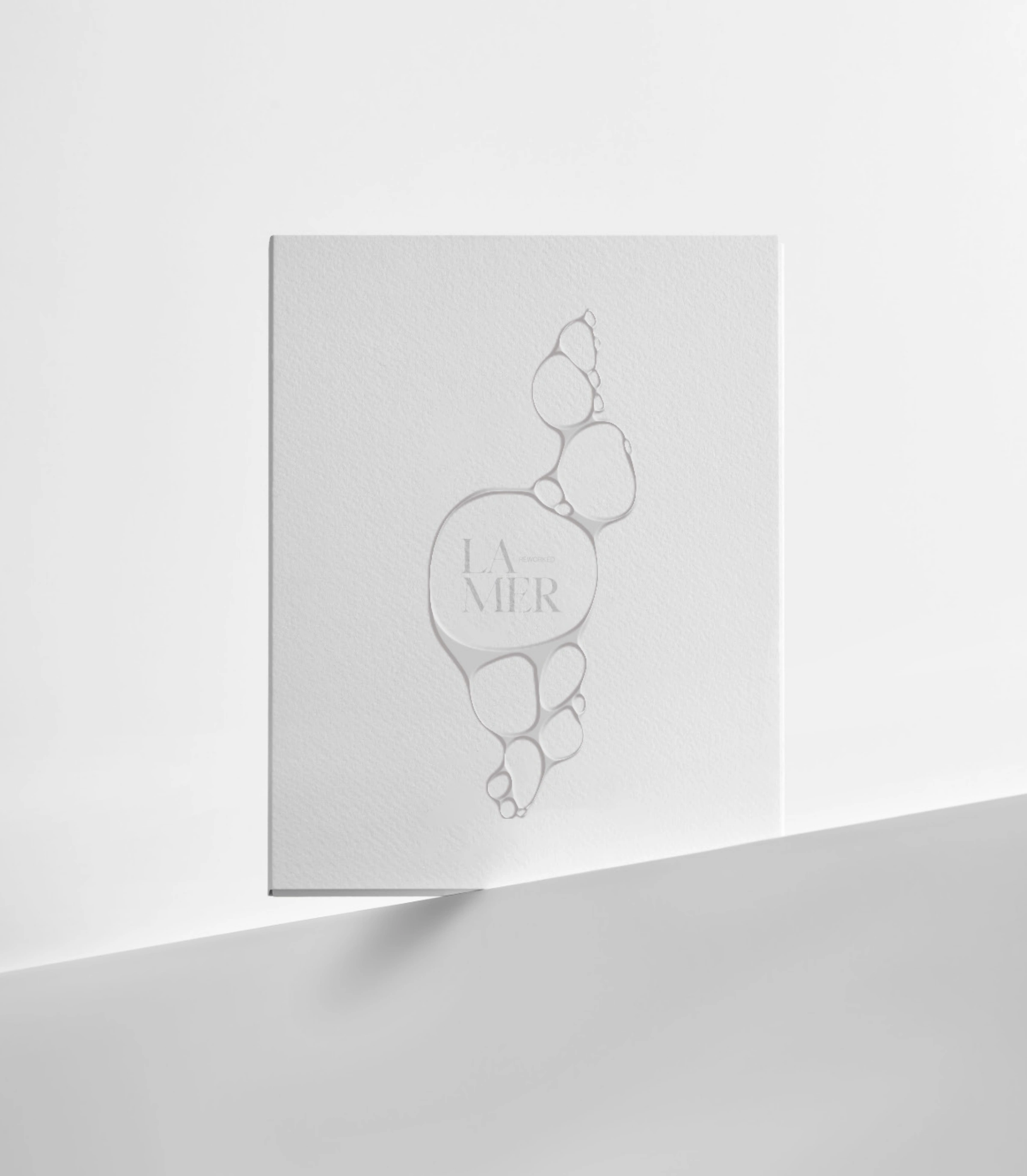 Proposition de packaging La Mer Reworked : étui blanc avec motif organique et logotype embossés.